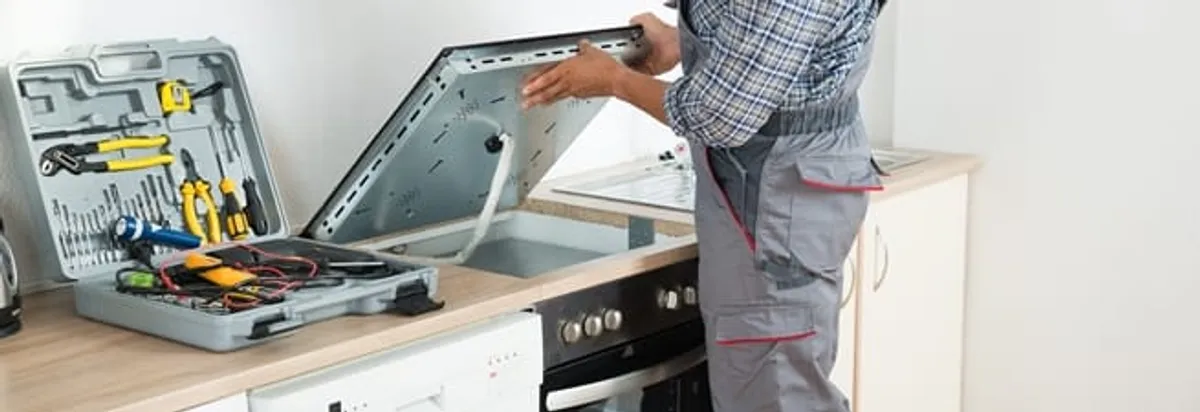 Cooktop repair technician lifting a built-in stovetop for service in San Diego, CA