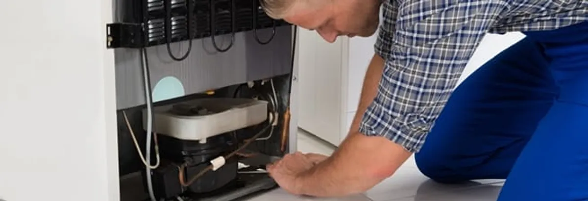 Refrigerator repair technician servicing the compressor and condenser area in San Diego, CA