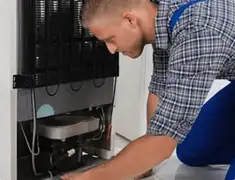 Refrigerator repair technician servicing the compressor and condenser area in San Diego, CA