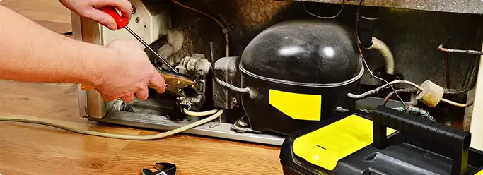 Refrigerator repair technician fixing the compressor and wiring in San Diego, CA